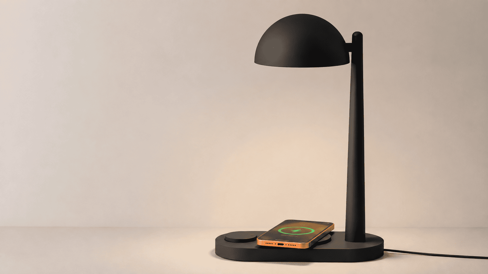 Lámpara negra de escritorio con cargador inalámbrico y smartphone naranja cargándose en la base
